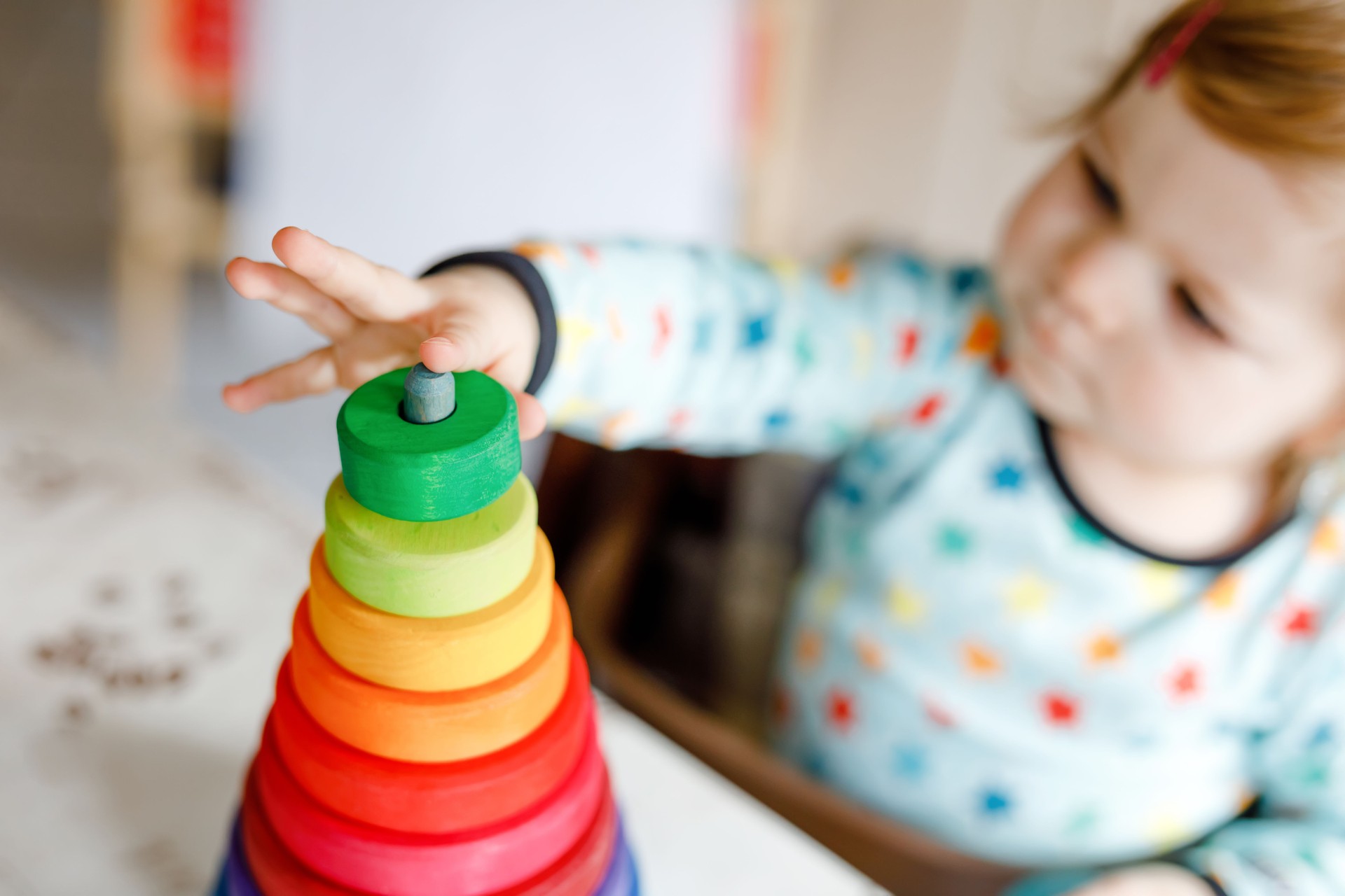 Cute beautiful little baby girl playing with educational toys at home or nursery, indoors. Happy healthy child having fun with colorful wooden rainbow toy pyramid. Kid learning different skills.